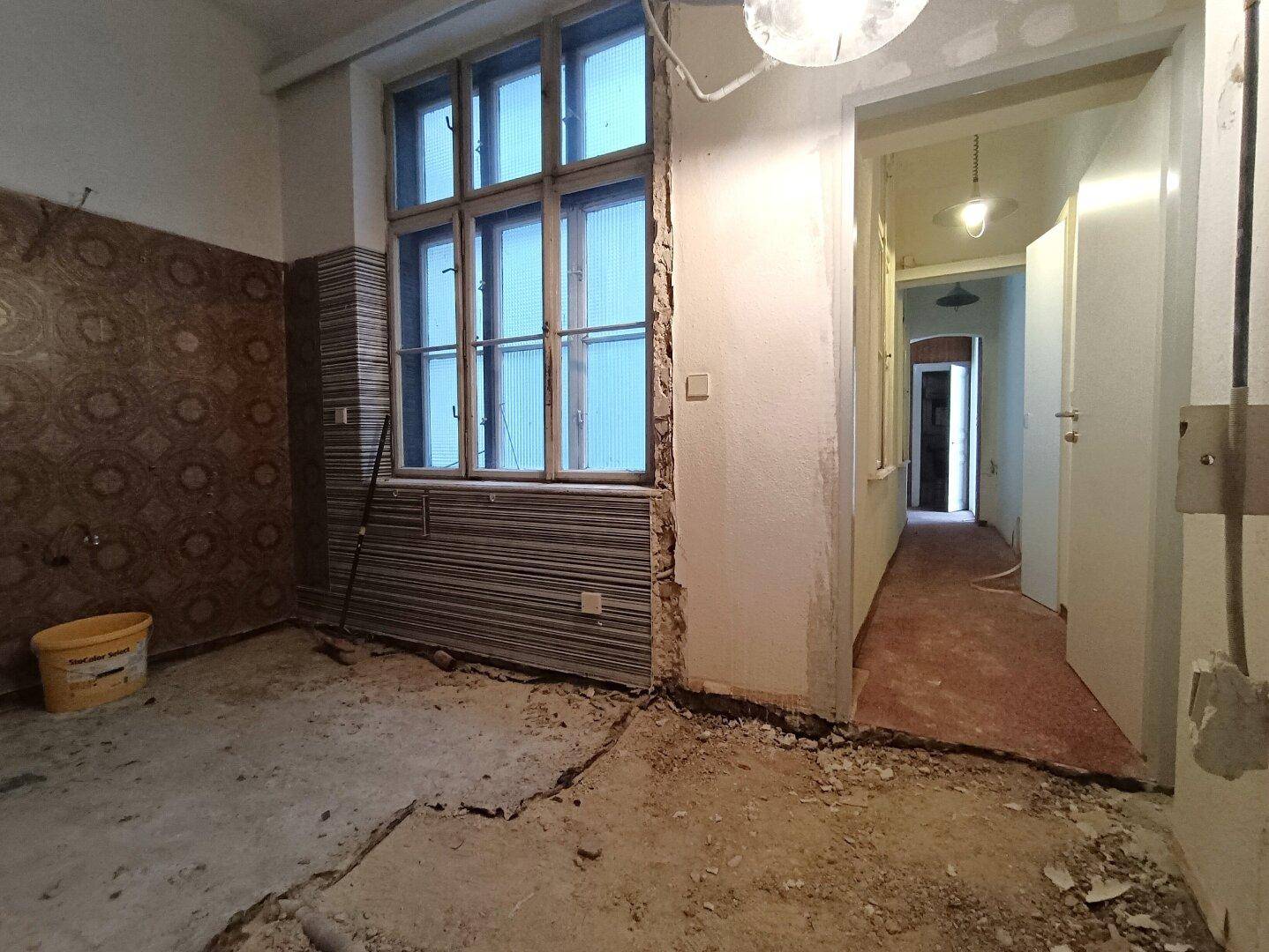 Renovierungsbedürftiger Raum mit freigelegten Wänden und Fenster, ideal für eine zukünftige Küche.