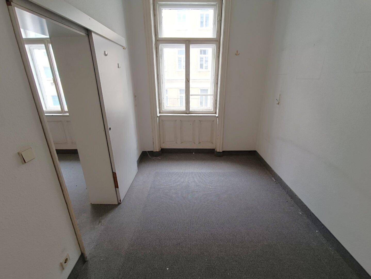 Helles Schlafzimmer mit Teppichboden und großem Fenster, das viel Tageslicht hereinlässt.