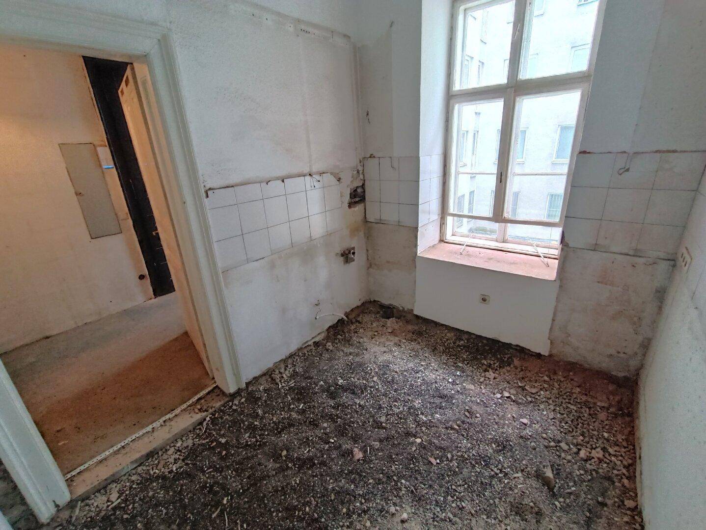 Renovierungsbedürftige Küche mit Fenster und alten Fliesenresten, bereit für den Umbau.