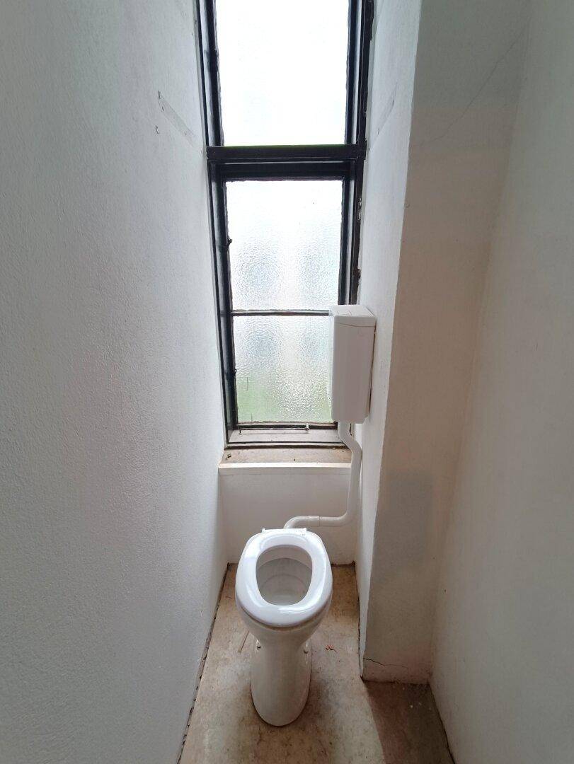 Kleines WC mit Fenster und einfacher Toilette, im schlichten Zustand.