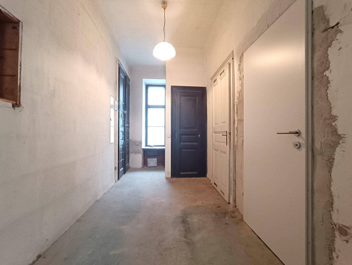 Langer Flur mit mehreren Türen und einem Fenster am Ende, im Renovierungszustand.
