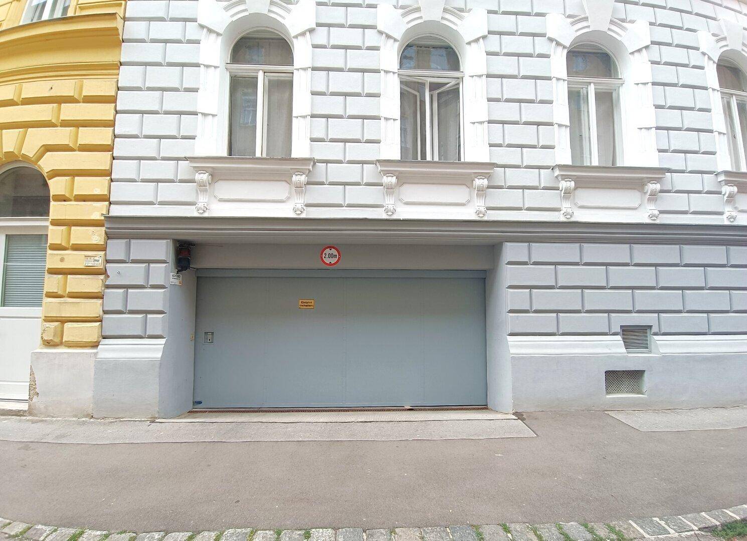 Eingang zu einer Tiefgarage mit Rolltor und Höhenbegrenzung in einem Stadtgebäude.