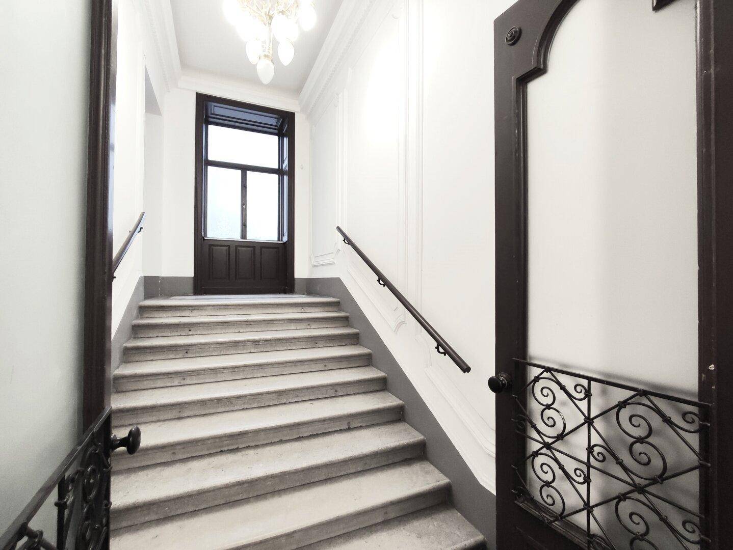 Elegantes Treppenhaus mit Steinstufen und schmiedeeisernem Geländer in einem Altbau.
