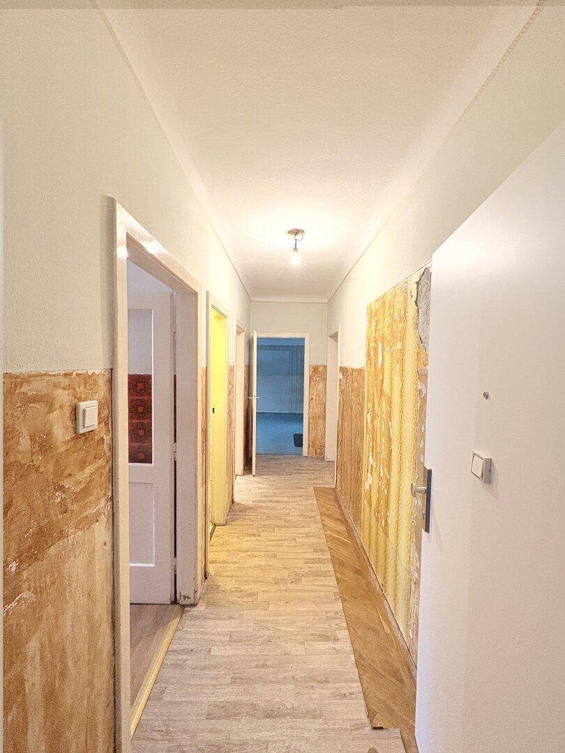 Langer Flur in Renovierung mit teilweise entfernten Tapeten und hellem Bodenbelag.