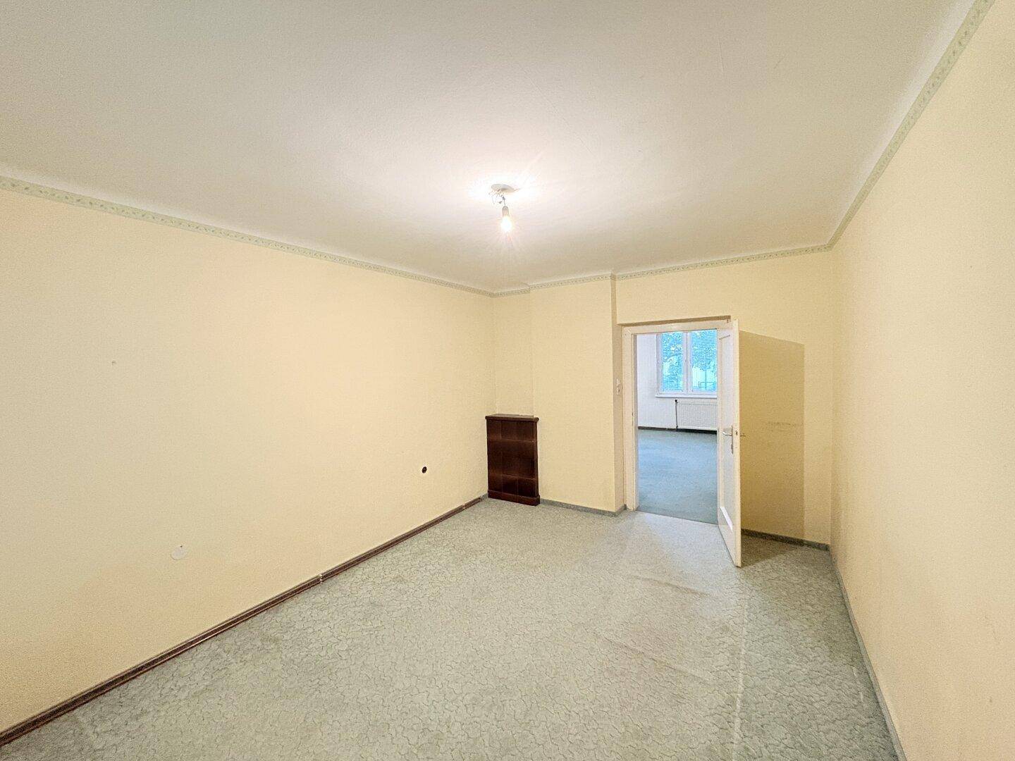 Weiterer heller Raum mit gelblichen Wänden, grauem Boden und einem kleinen Schrank.