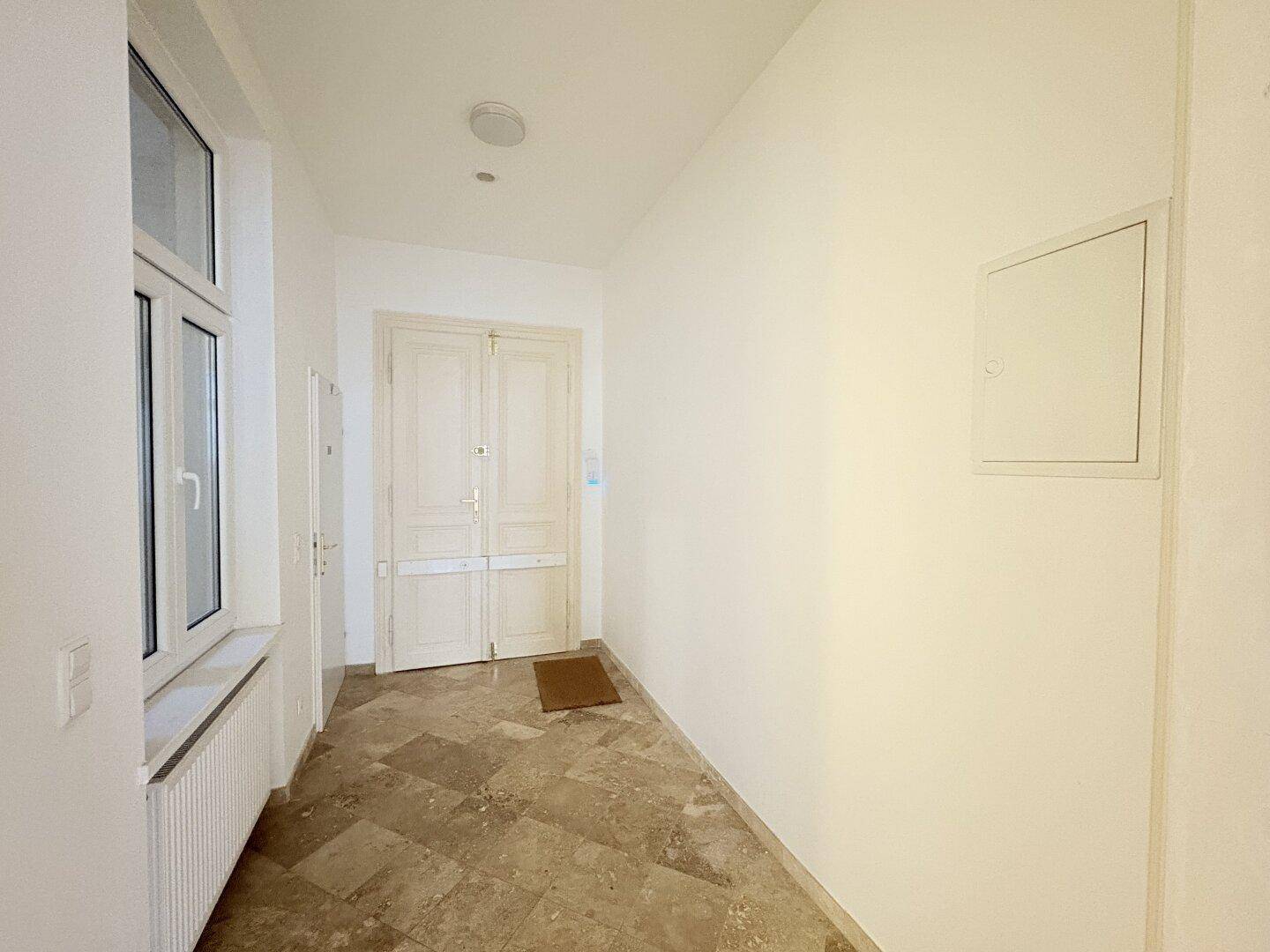 Heller Flur mit Fliesenboden und einer großen Eingangstür, die in die Wohnung führt.