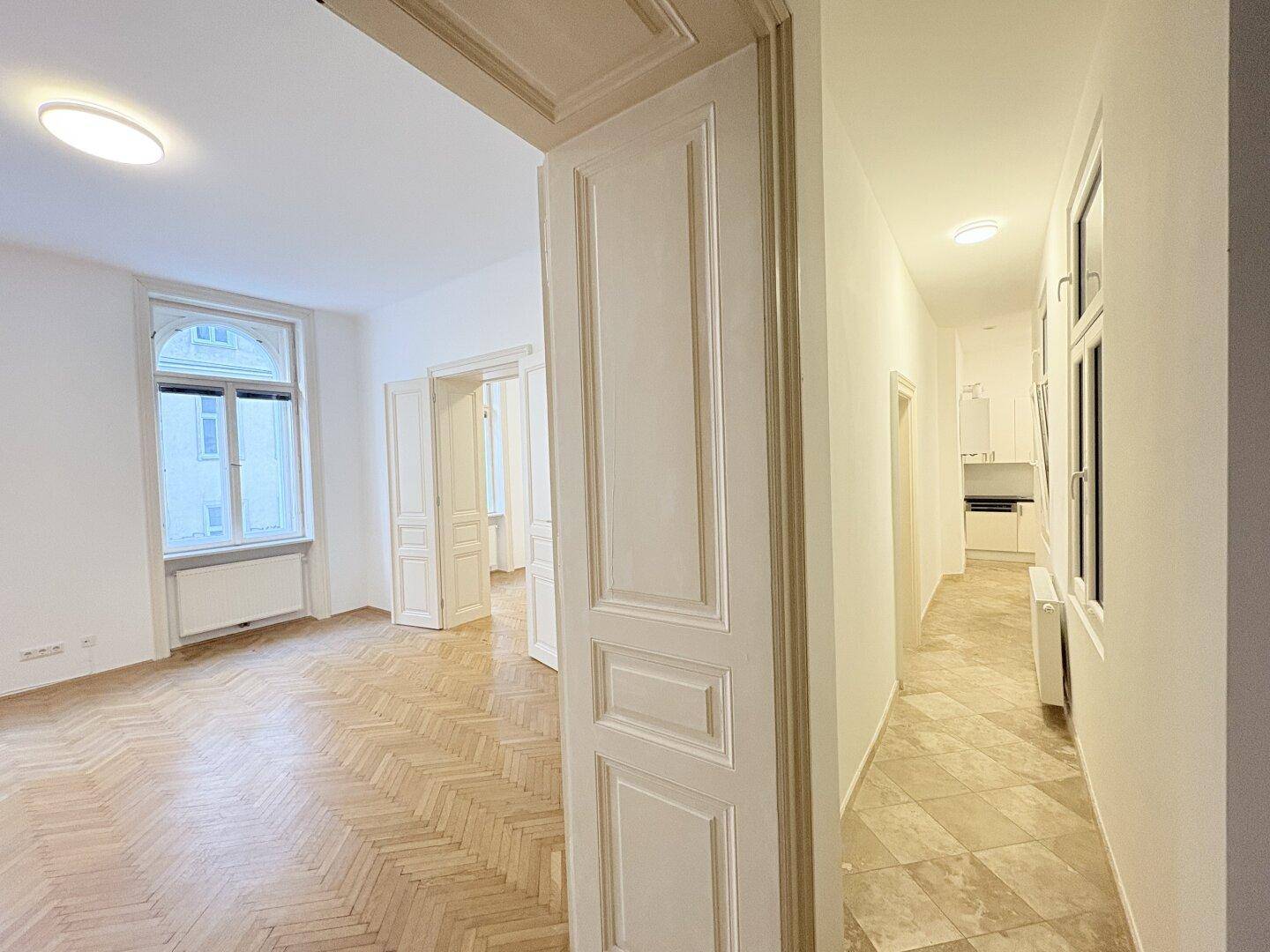Heller Flur mit Fliesenboden, der zu einem geräumigen Zimmer mit Parkett führt.
