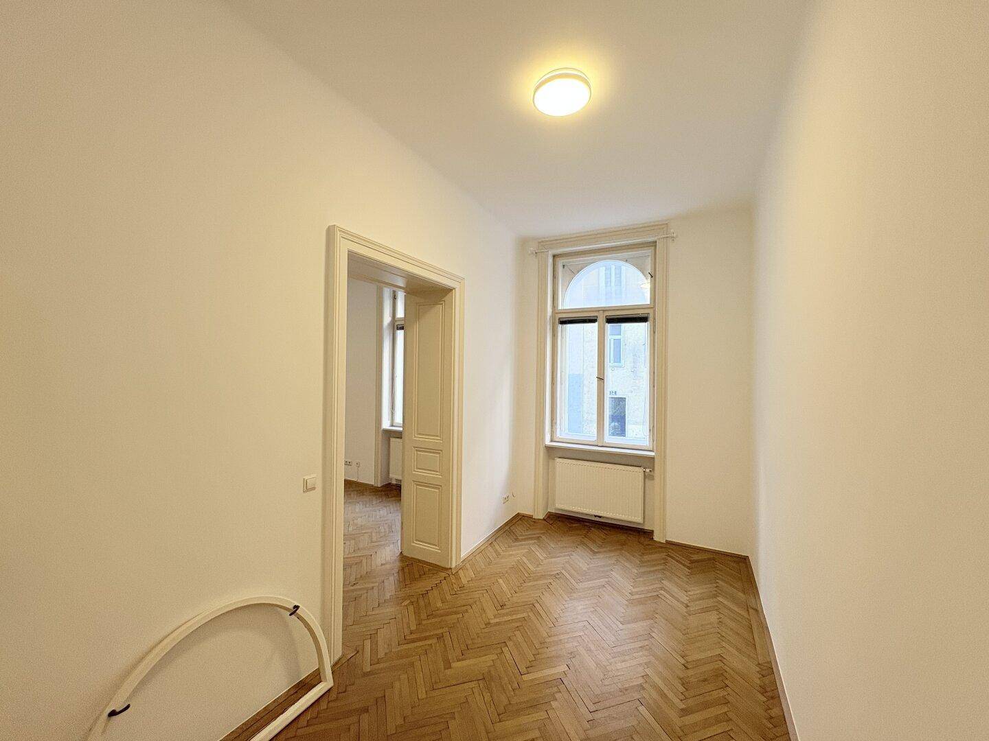 Kleineres Zimmer mit Fischgrätparkett und einem hohen Fenster, ideal als Schlafzimmer.