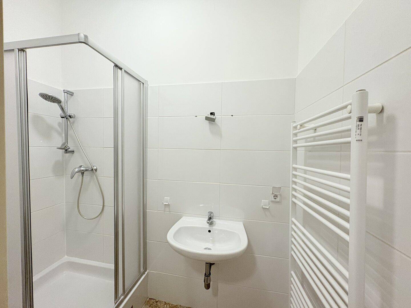 Kleines Badezimmer mit Duschkabine, Waschbecken und beheiztem Handtuchhalter.