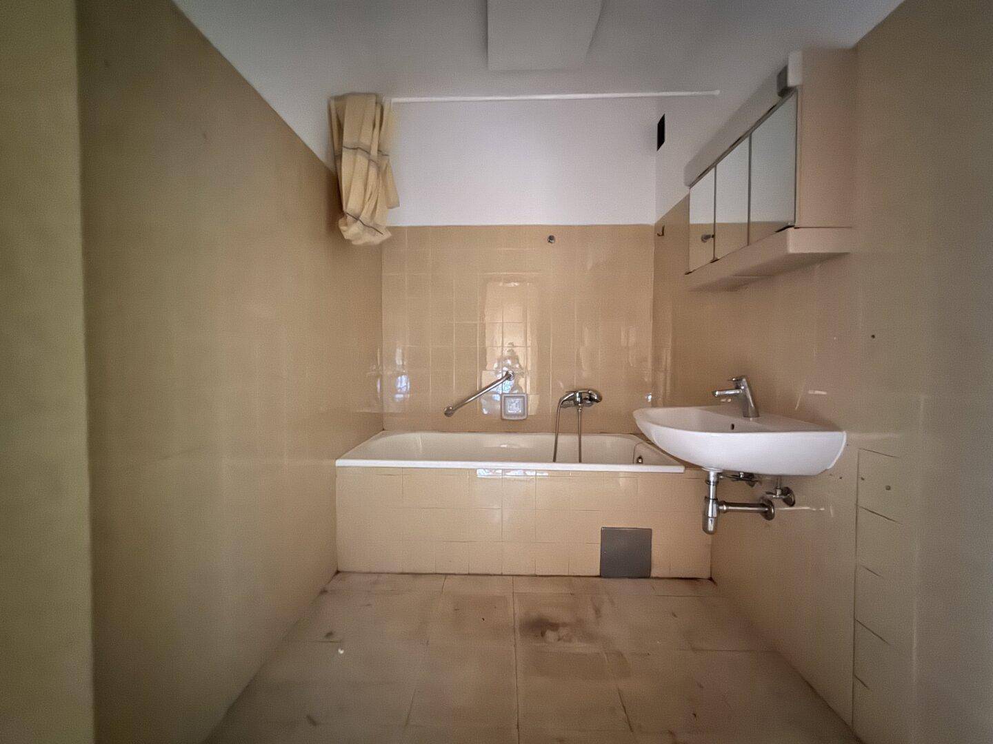 Badezimmer mit Badewanne, Waschbecken und Spiegelschrank, ausgestattet mit beigen Fliesen.