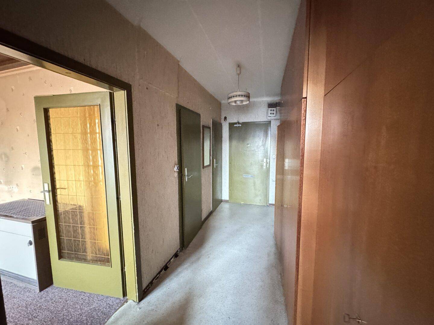 Langer Flur mit Holzverkleidung, älterer Tapete und mehreren Türen zu den angrenzenden Räumen.