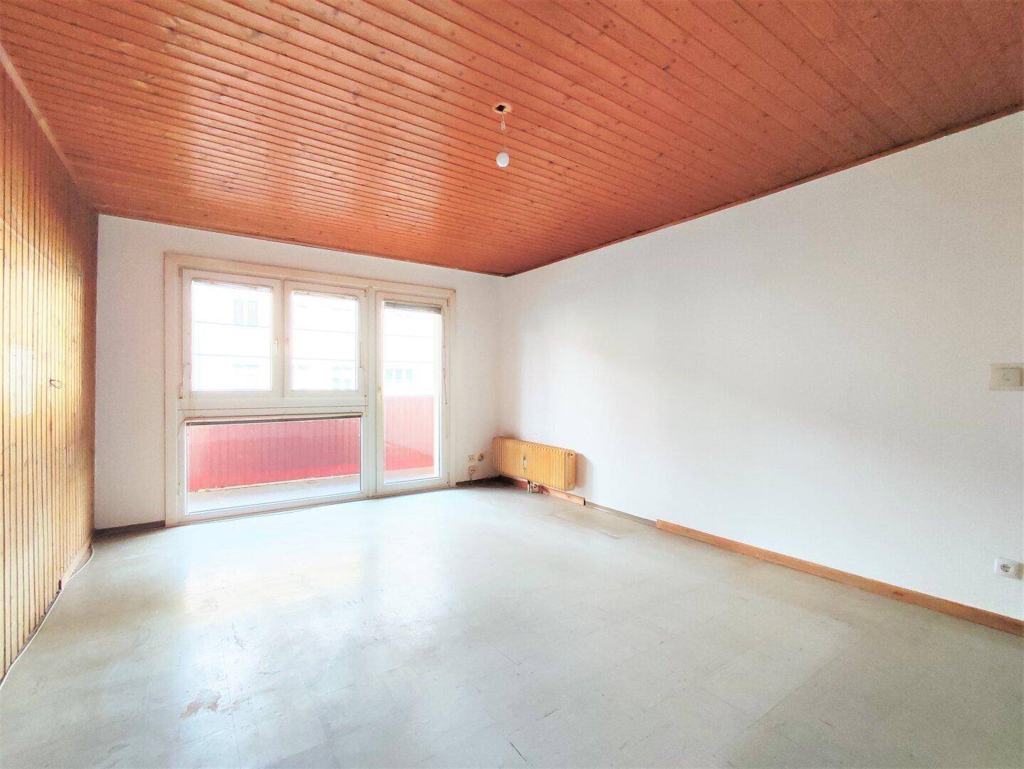Heller, leerer Raum mit Holzdecke, Holzpaneelen und großem Fenster mit Balkonzugang.