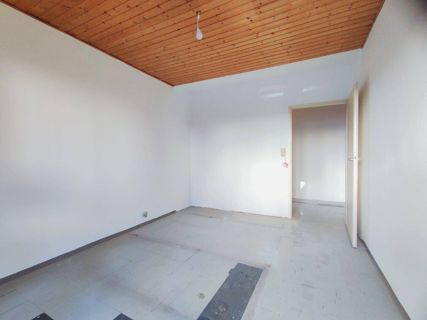 Leerer Raum mit Holzdecke und weiß gestrichenen Wänden, bereit zur individuellen Gestaltung.