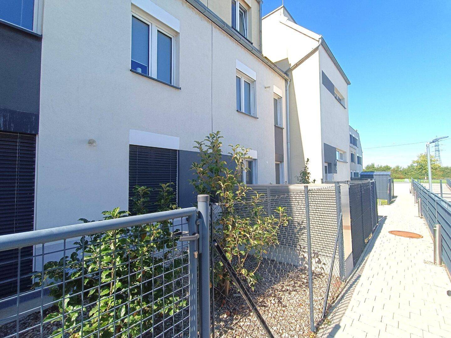 Moderne Fassade eines Mehrfamilienhauses mit großen Fenstern und Jalousien.