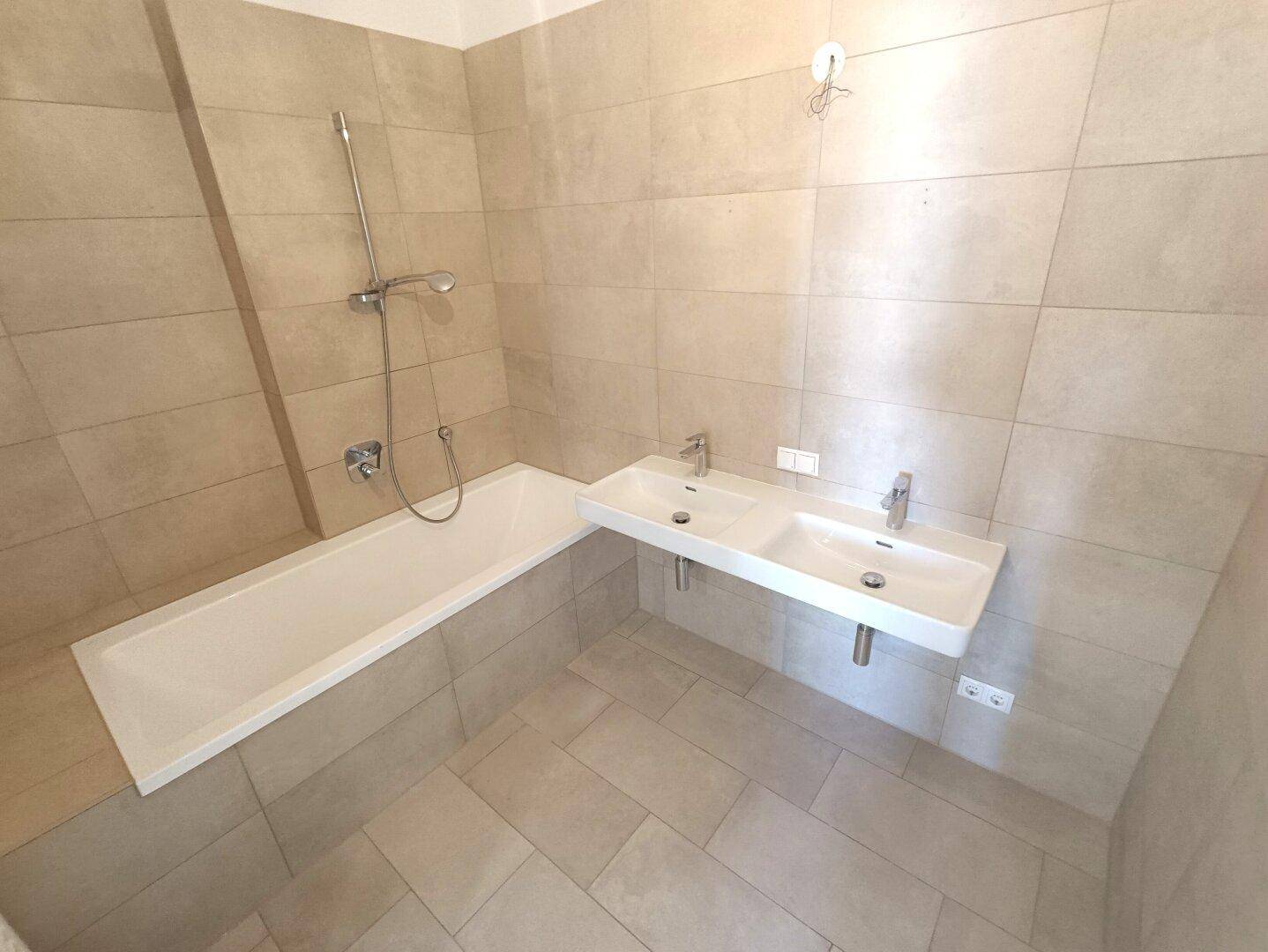 Helles Badezimmer mit Badewanne, Doppelwaschbecken und modernen beigefarbenen Fliesen.