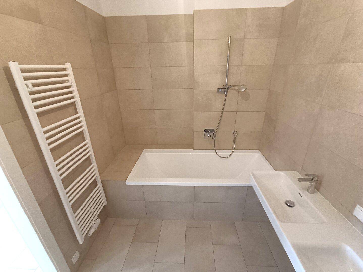 Funktionales Badezimmer mit Badewanne, Waschbecken und beheiztem Handtuchhalter.