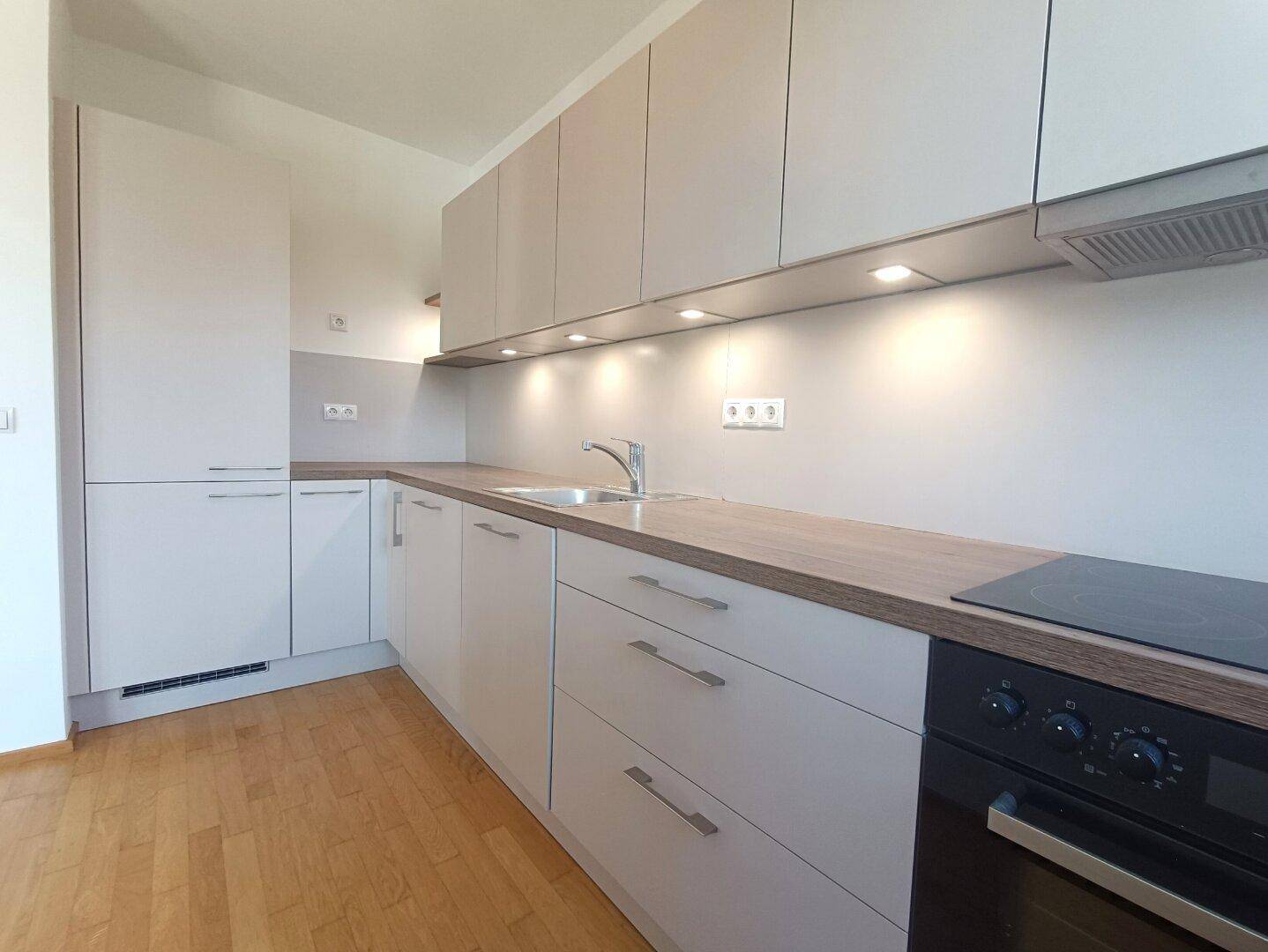 Moderne Einbauküche mit hellen Schränken, Holzoptik-Arbeitsplatte und integrierten Geräten.