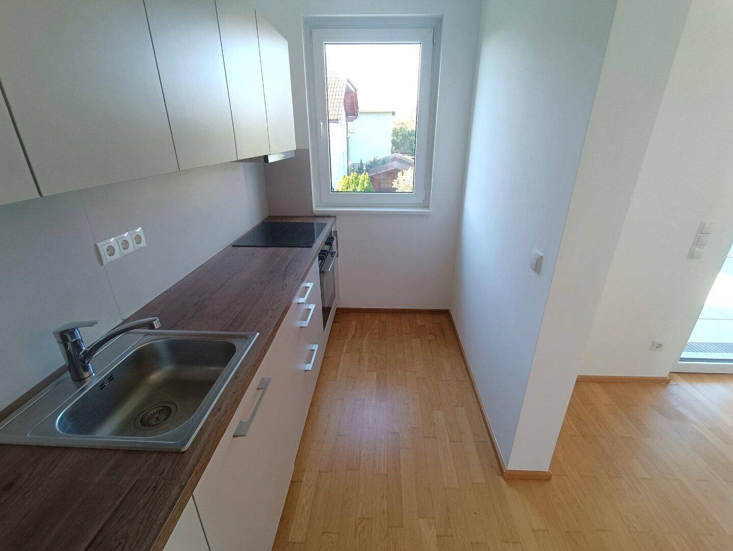 Kompakte Küche mit Fenster, Einbauschränken und Arbeitsplatte in Holzoptik.