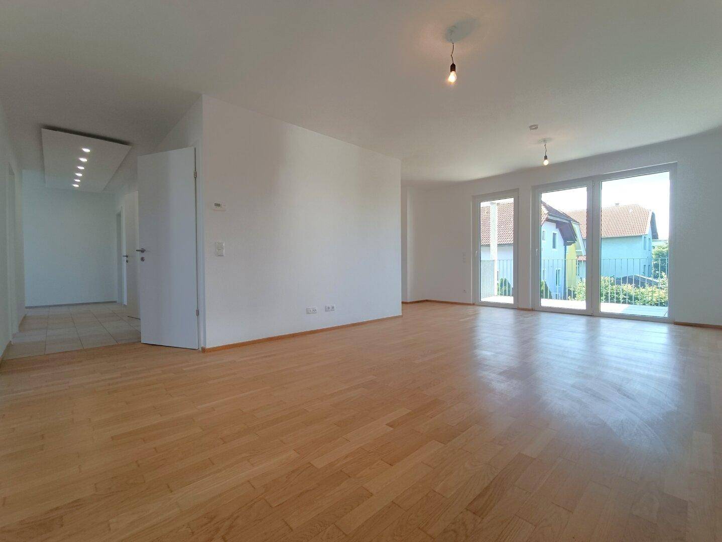 Lichtdurchfluteter Wohn-Essbereich mit Parkettboden und Zugang zum Balkon.