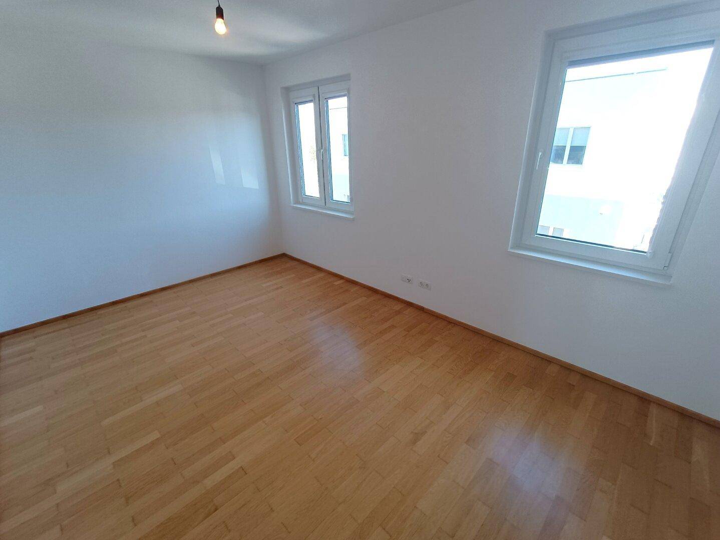 Helles Schlafzimmer mit Parkettboden und zwei Fenstern für viel Tageslicht.