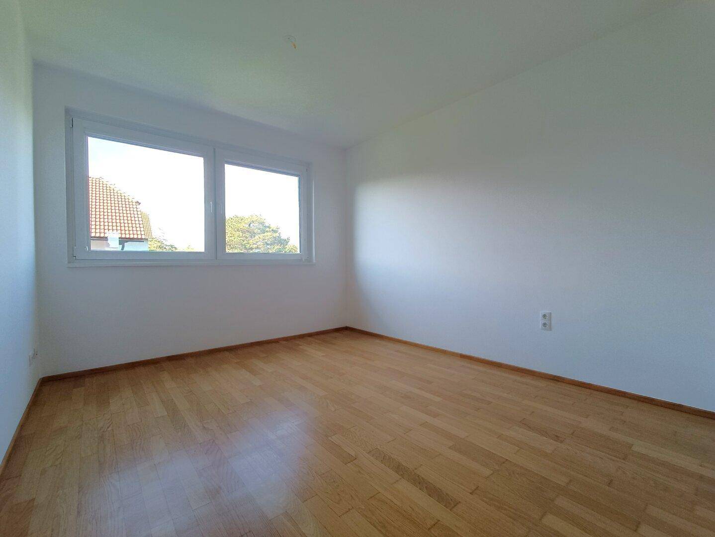 Geräumiges Schlafzimmer mit Parkettboden und Blick ins Grüne durch zwei Fenster.