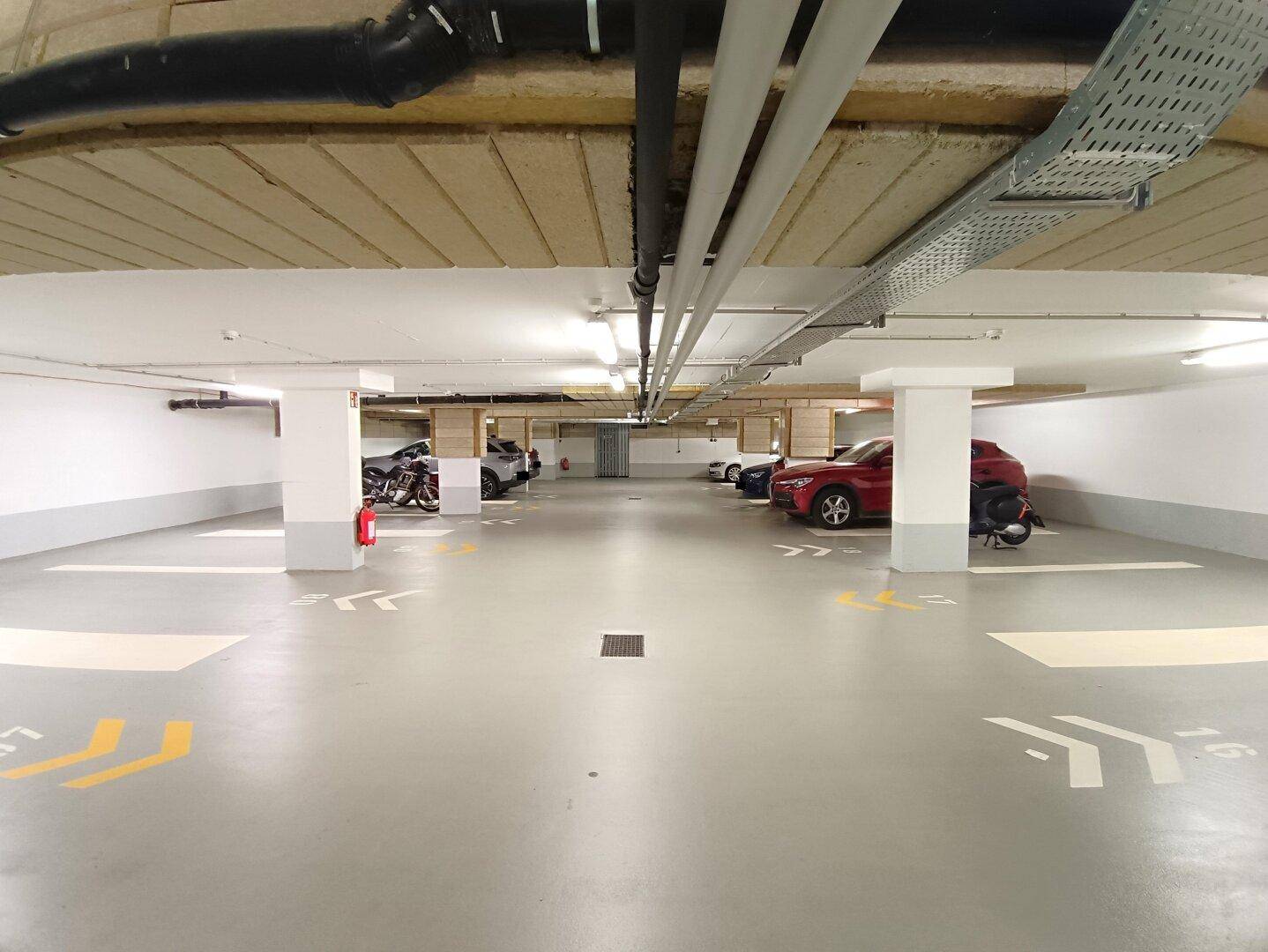 Weitläufige Tiefgarage mit mehreren geparkten Fahrzeugen und klar gekennzeichneten Stellplätzen unter einer funktionalen Decke.