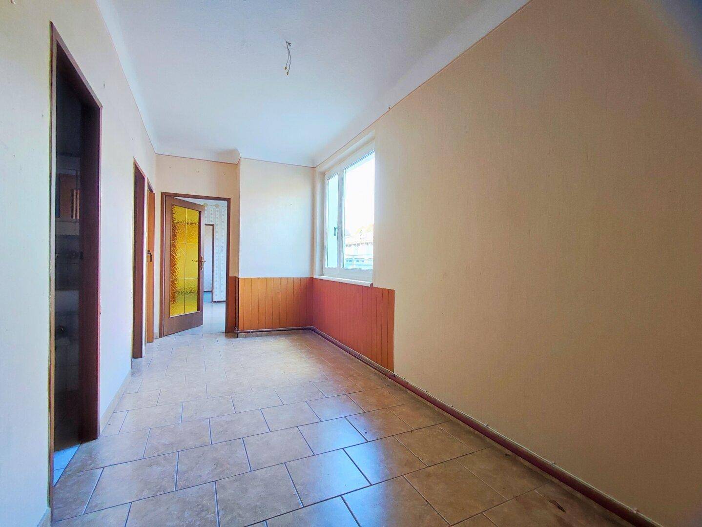 Heller Flur mit Fliesenboden, Fenster und mehreren Türen zu angrenzenden Räumen.
