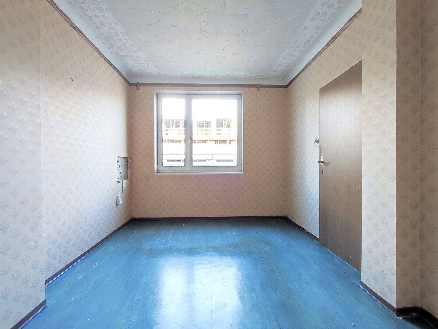 Leerer Raum mit blauer Bodenfarbe und gemusterter Tapete, der Renovierung benötigt.