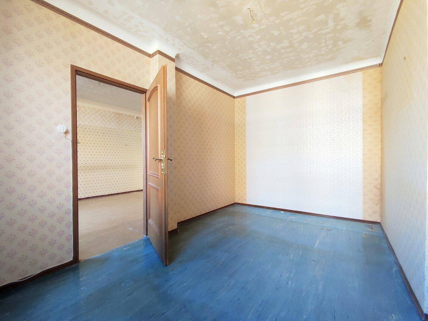 Leerer Raum mit blauer Bodenfarbe und gemusterter Tapete, bereit zur Renovierung.