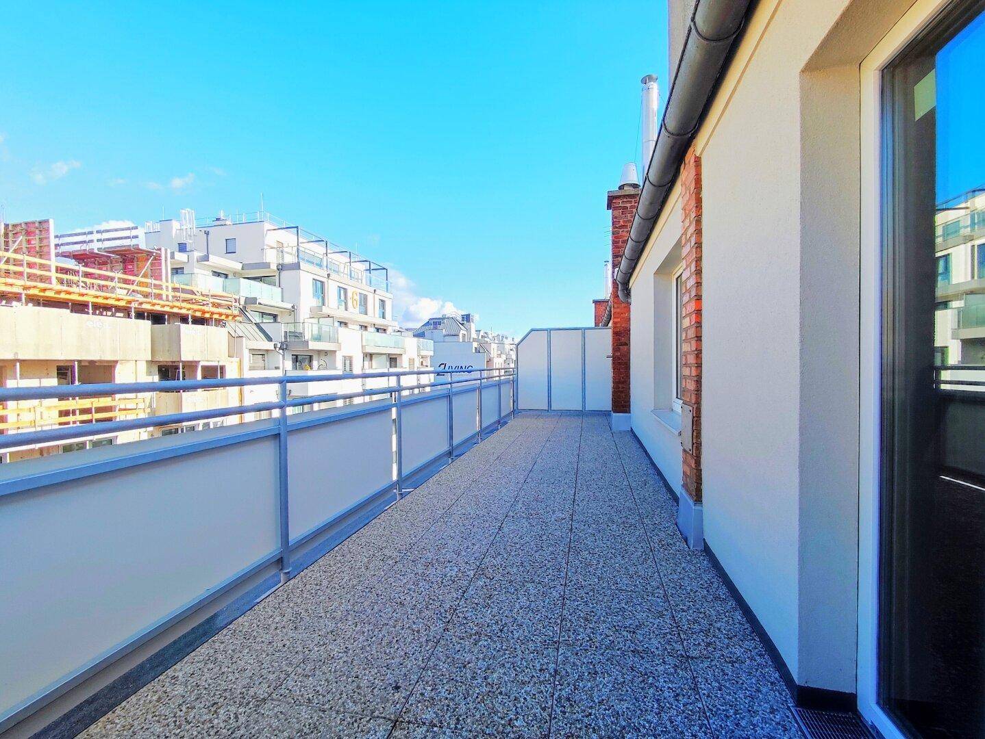 Weitläufige Dachterrasse mit Blick auf die Stadt und angrenzende Neubauten.