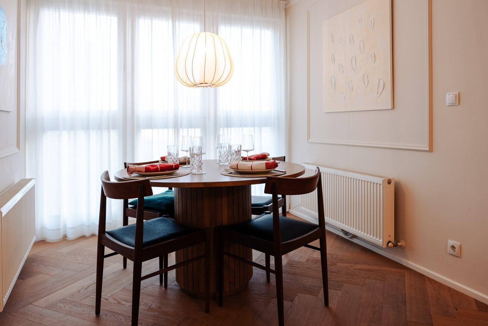 Gemütlicher Essbereich mit rundem Holztisch, modernen Stühlen und großen Fenstern für viel Tageslicht.
