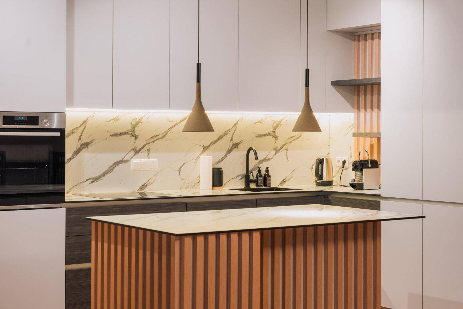 Moderne Küche mit weißen Schränken, Marmor-Rückwand, Kücheninsel und hochwertigen Geräten.
