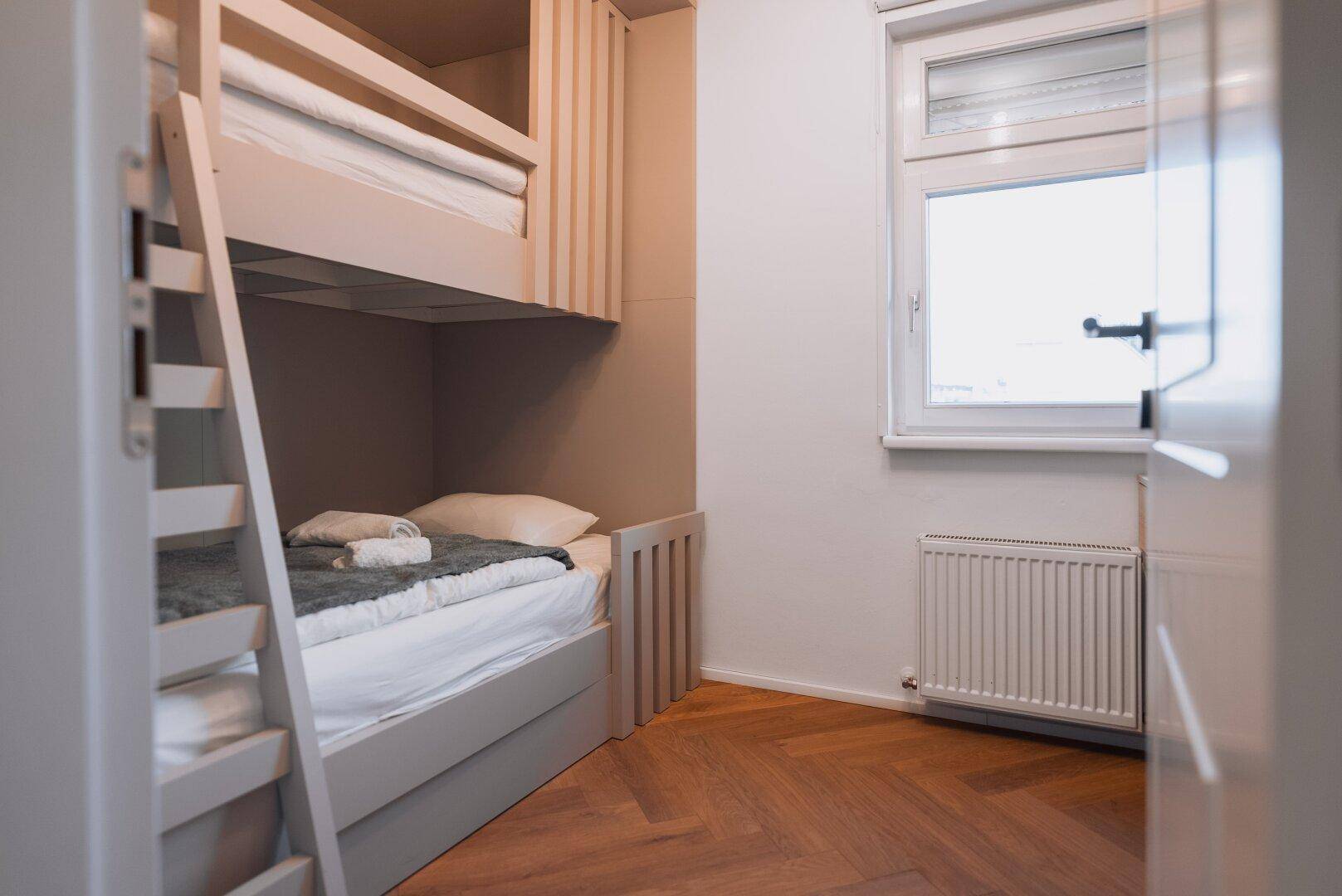 Kinderzimmer mit Etagenbett, Fischgrätparkett und einem Fenster für natürliches Licht.