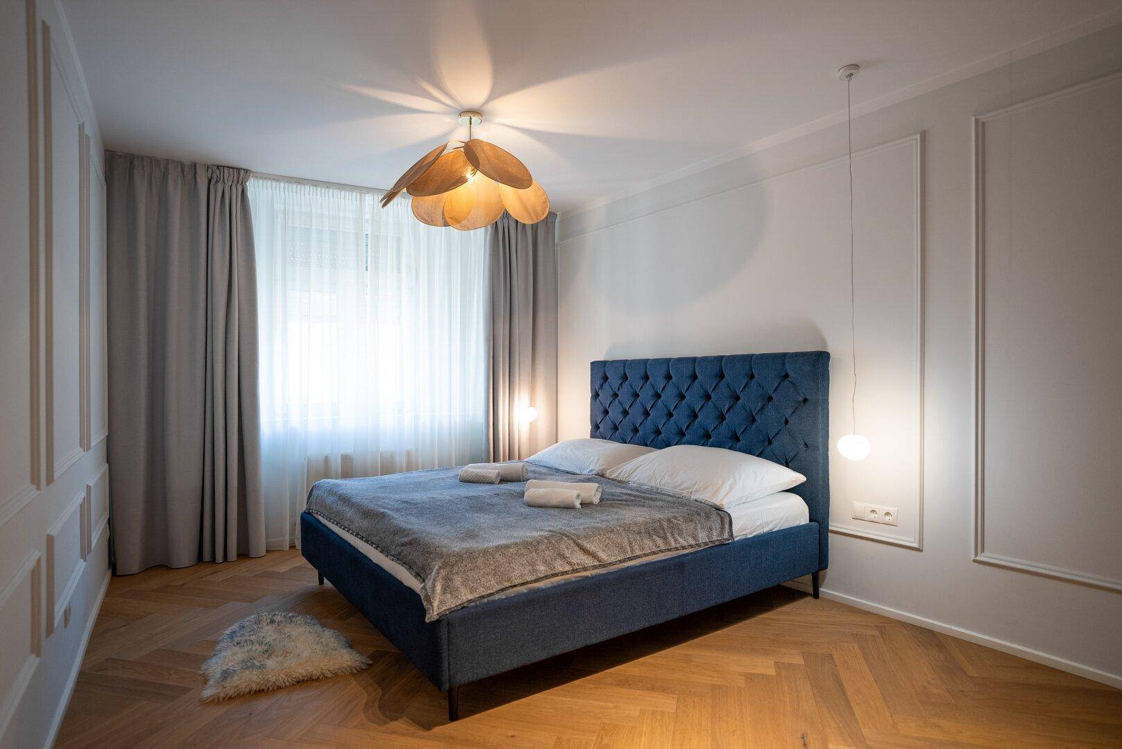Helles Schlafzimmer mit Doppelbett, Fischgrätparkett und dekorativer Wandgestaltung.