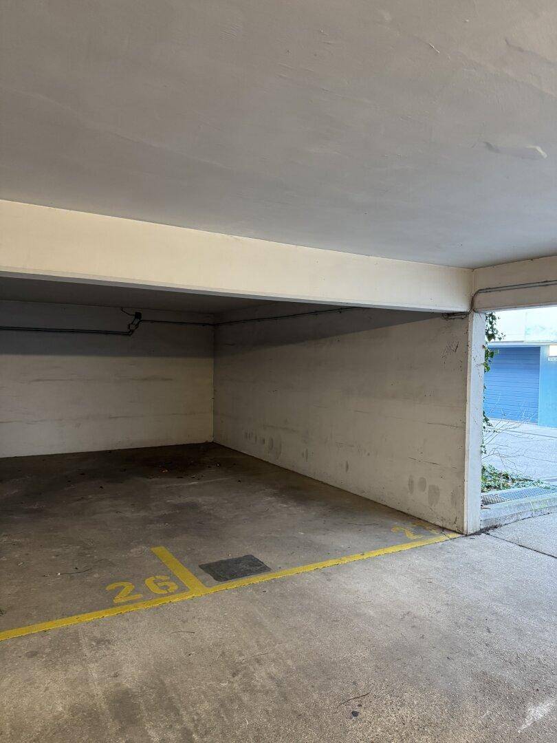 Einzelner, leerer Parkplatz in einer überdachten Parkgarage mit Betonboden und gelben Markierungen.