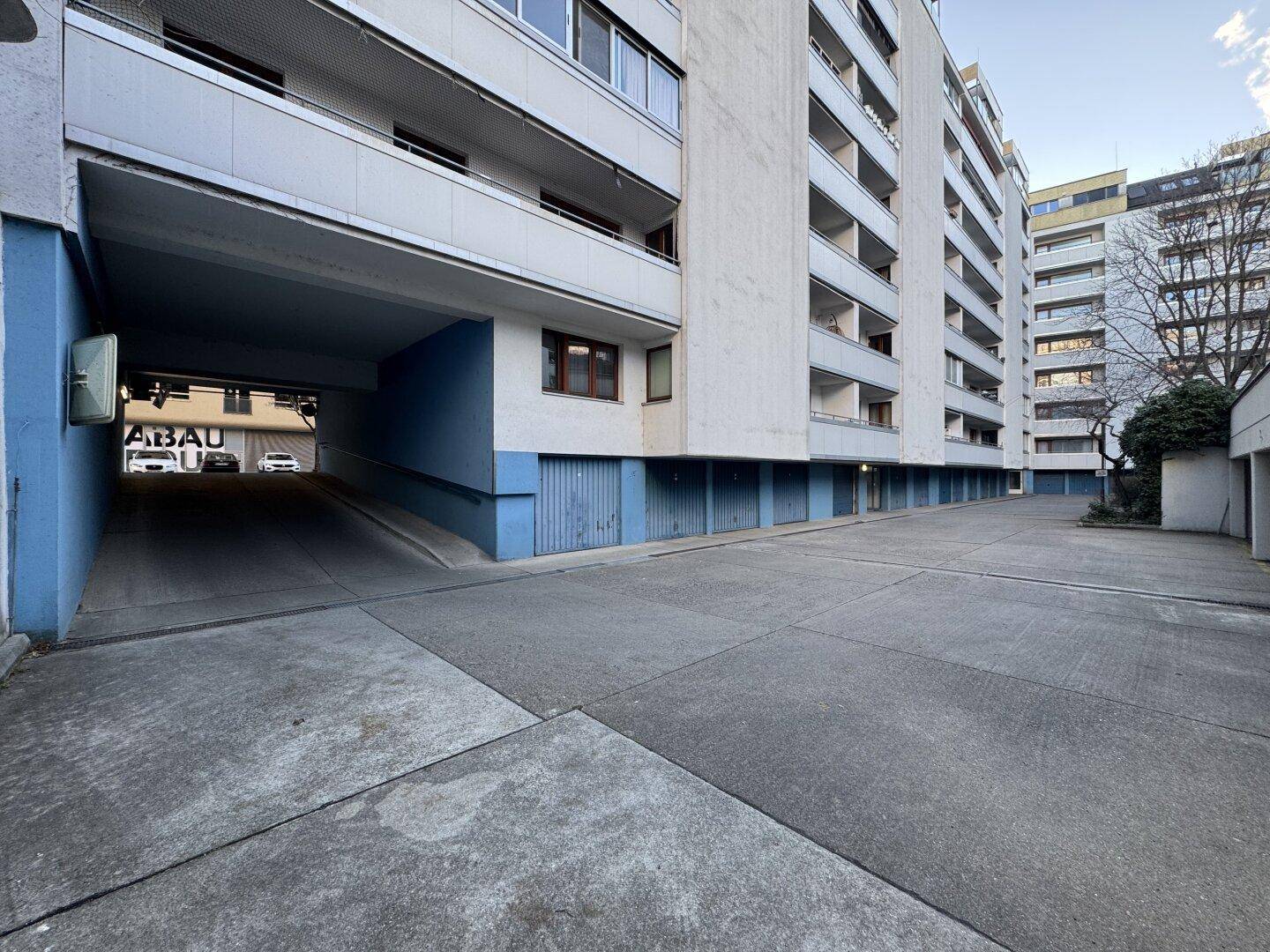Weitläufige Ansicht der Zufahrt zur Tiefgarage und des Wohngebäudes mit Balkonen und Garagentoren.