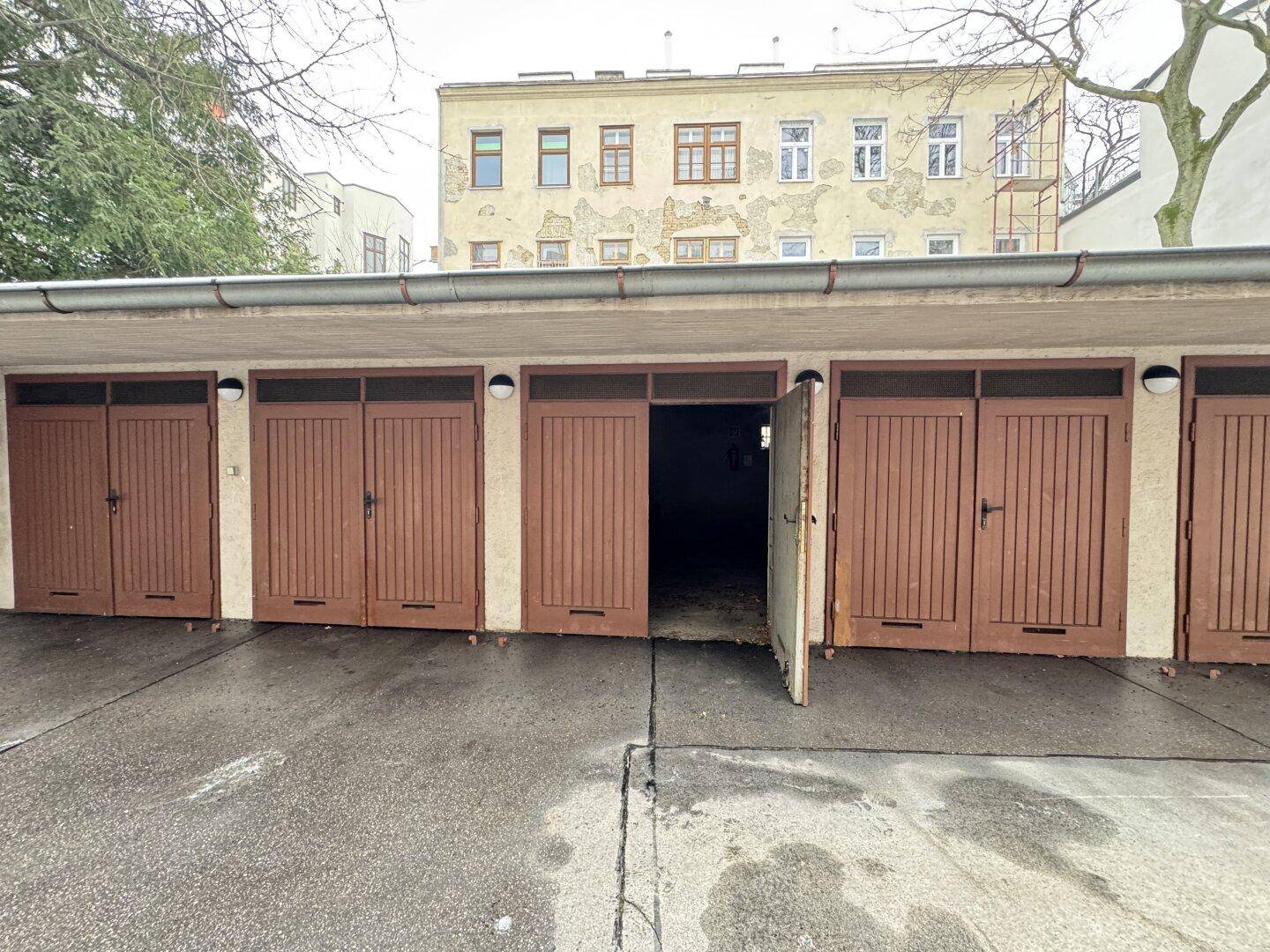 Nahaufnahme einer Reihe von Garagen mit braunen Holztoren und einem geöffneten Garagentor.