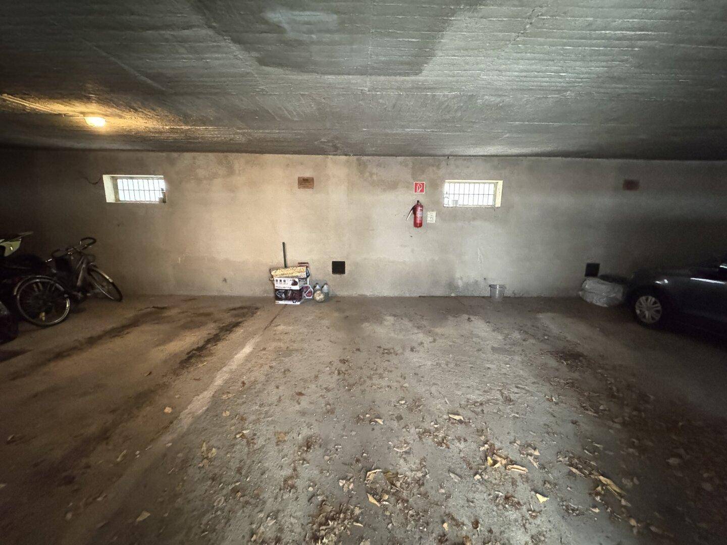 Dunkle Tiefgarage oder Kellerraum mit Betonwänden, einem Auto und Fahrrädern.