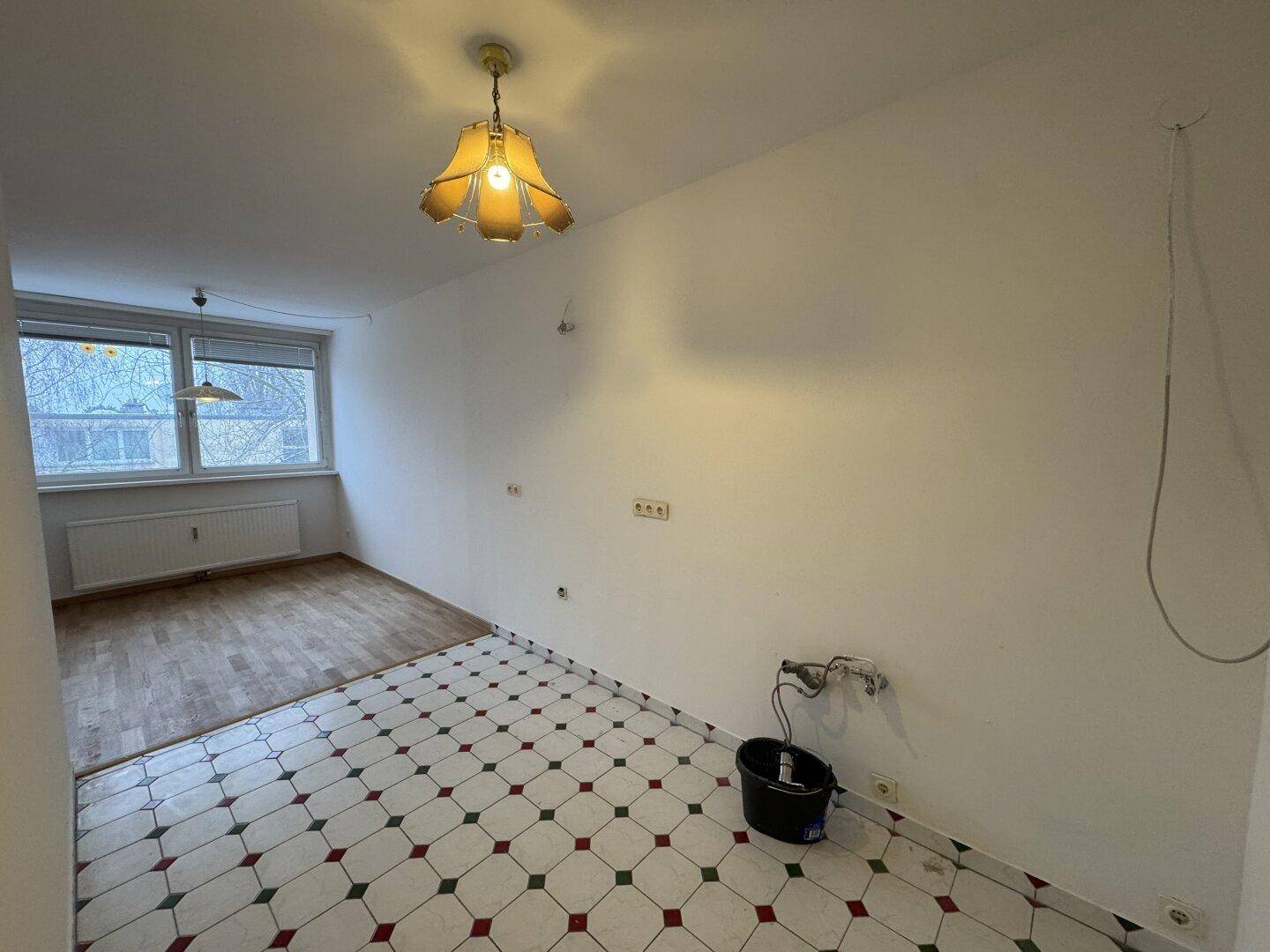 Leerer Küchenbereich mit Fliesenboden und Anschlüssen, bereit für die Installation einer neuen Einbauküche.