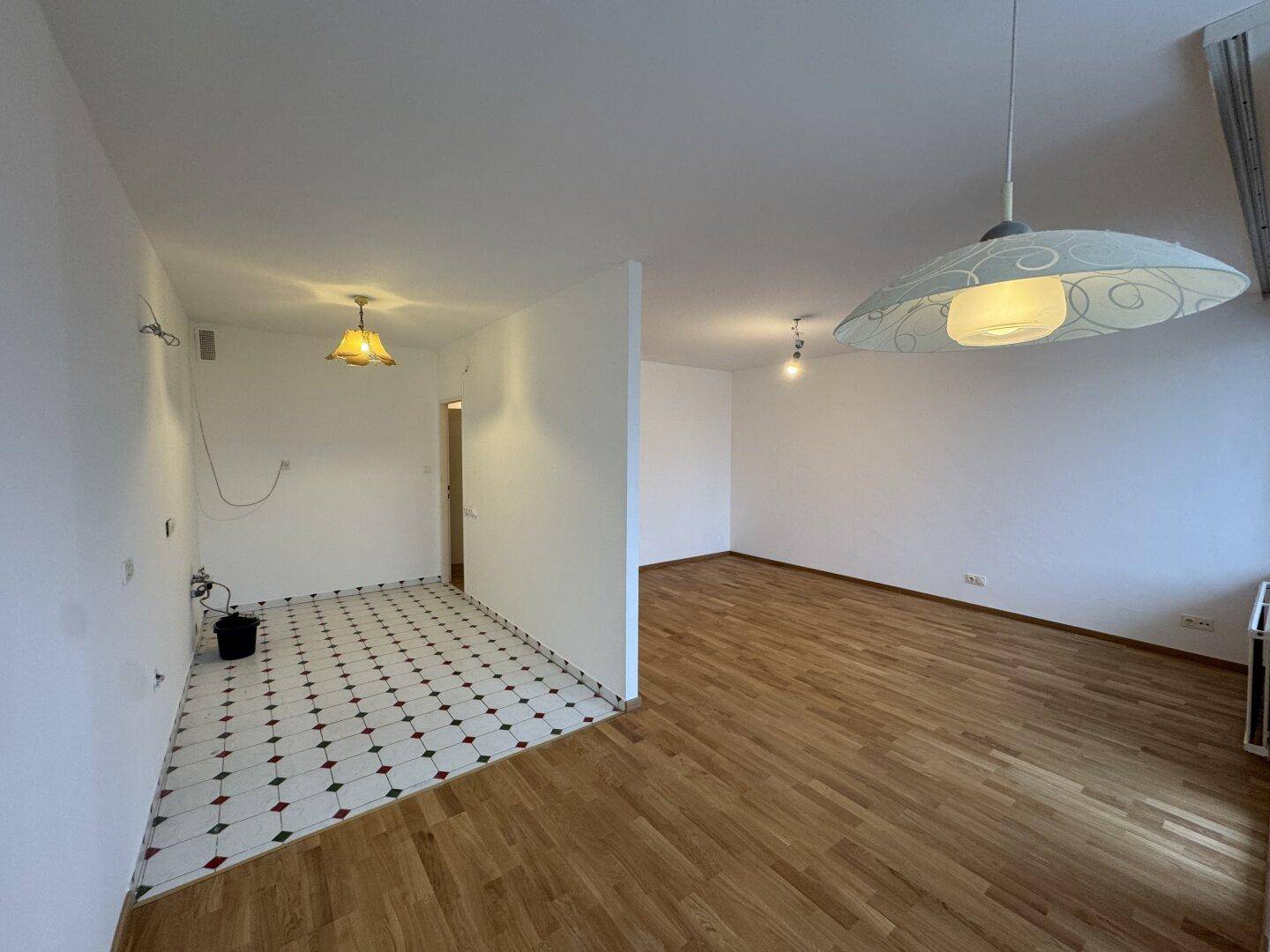 Geräumiger, leerer Wohnbereich mit Parkettboden und angrenzendem gefliesten Küchenbereich, bereit zur Gestaltung.