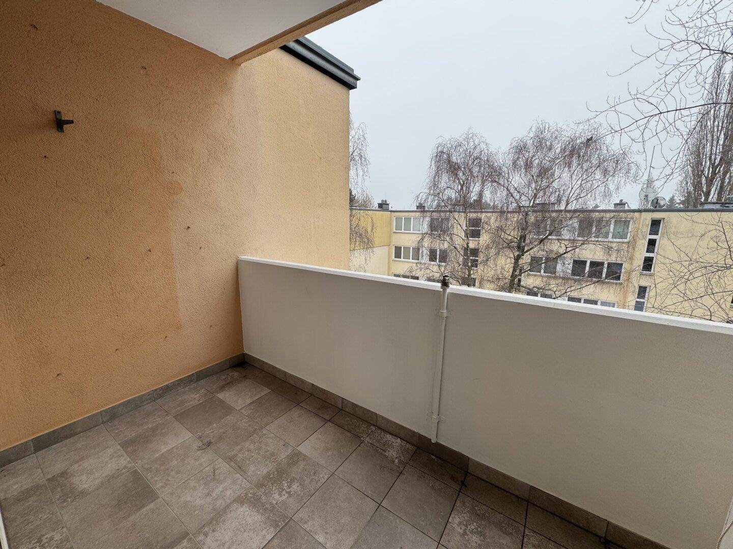 Kleiner Balkon mit Fliesenboden und Blick auf die umliegenden Gebäude und Bäume.