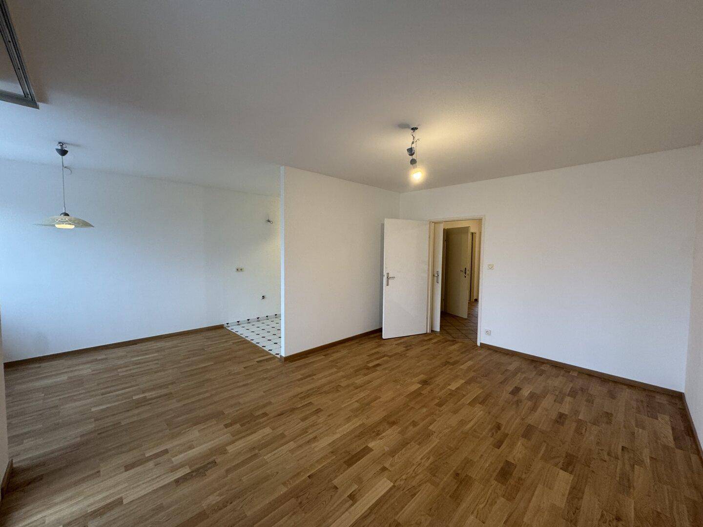 Heller, leerer Wohnbereich mit Parkettboden und Zugang zu weiteren Zimmern, ideal für individuelle Gestaltung.