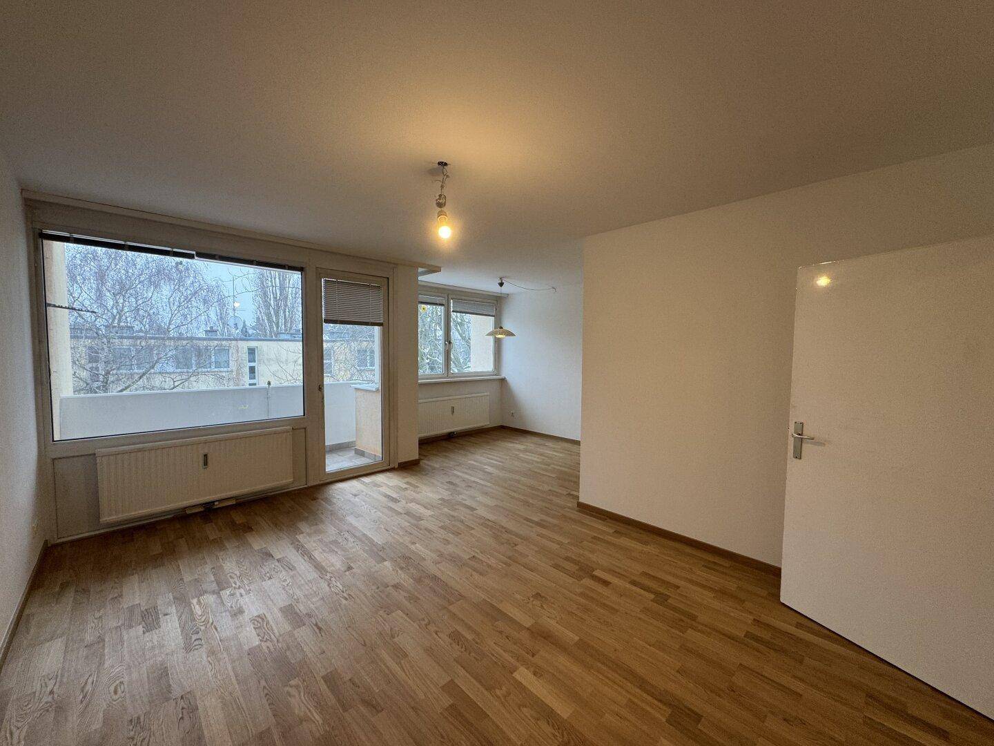 Geräumiger, leerer Wohnbereich mit Parkettboden und direktem Zugang zu einem Balkon.