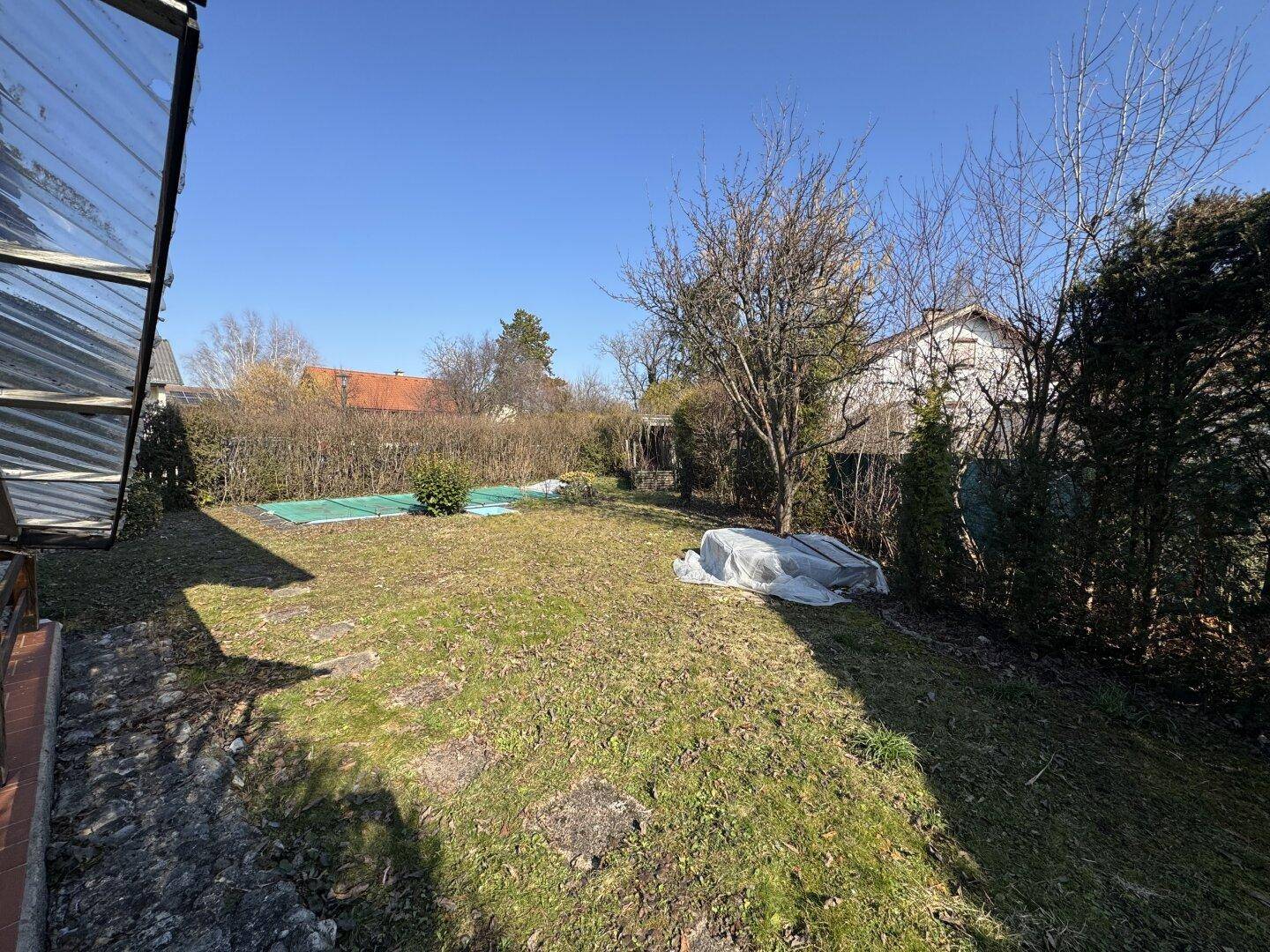Weitläufiger Garten mit Rasenfläche, abgedecktem Pool und Gewächshaus am Rand.