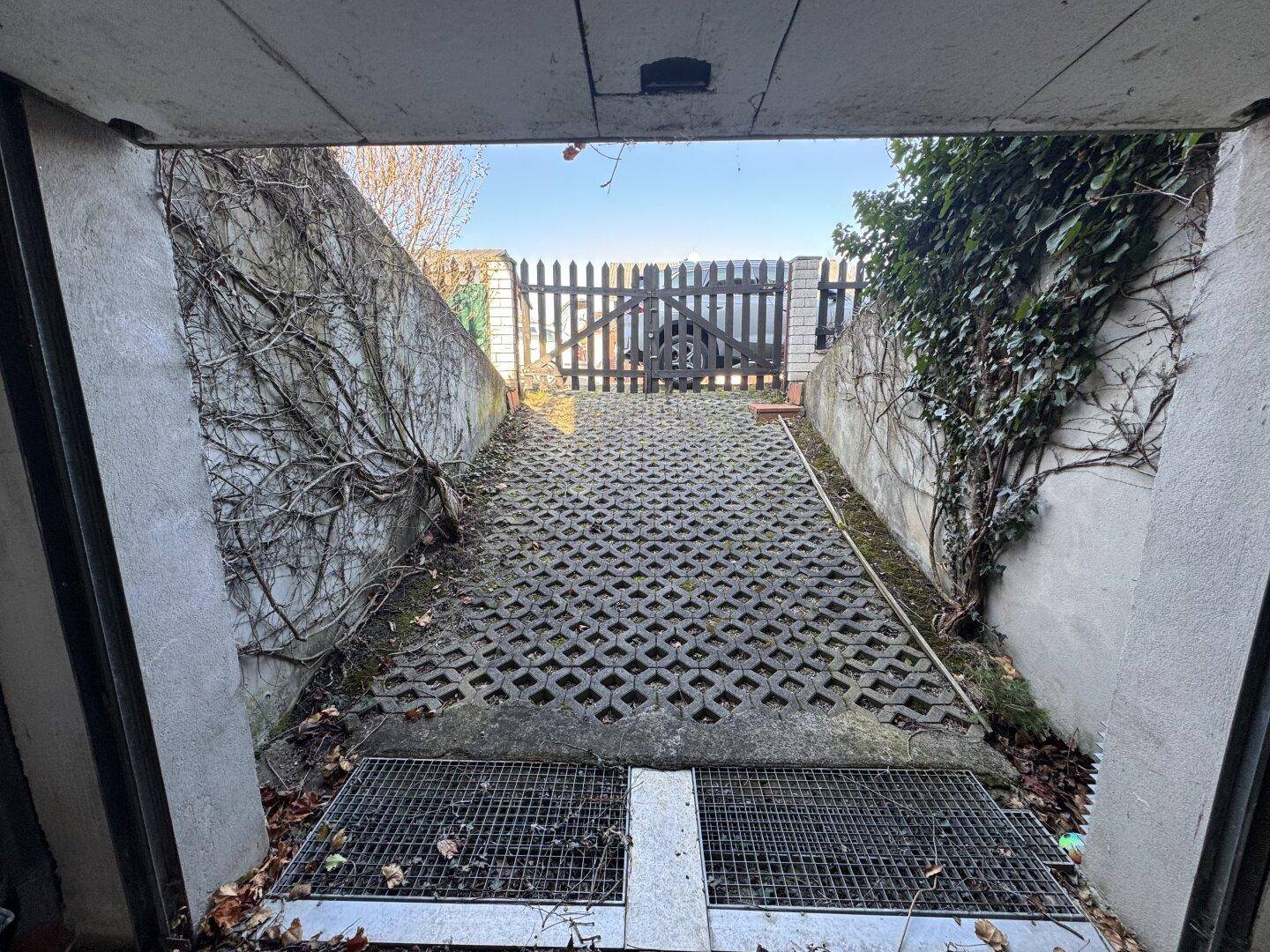 Zufahrt zur Tiefgarage mit Betonpflastersteinen und Holzzaun im Hintergrund.