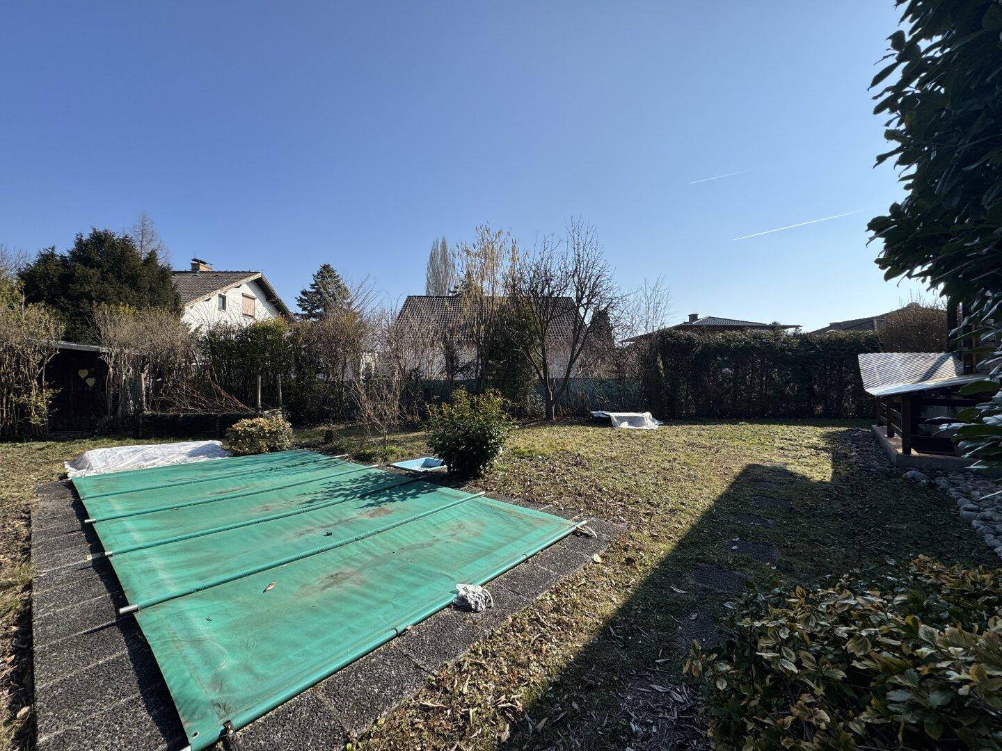 Großer Gartenbereich mit Rasenfläche und abgedecktem Pool unter blauem Himmel.
