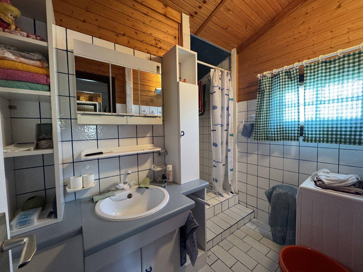 Helles Badezimmer mit Dusche, Waschbecken und Waschmaschine, gefliest in Weiß und Blau.