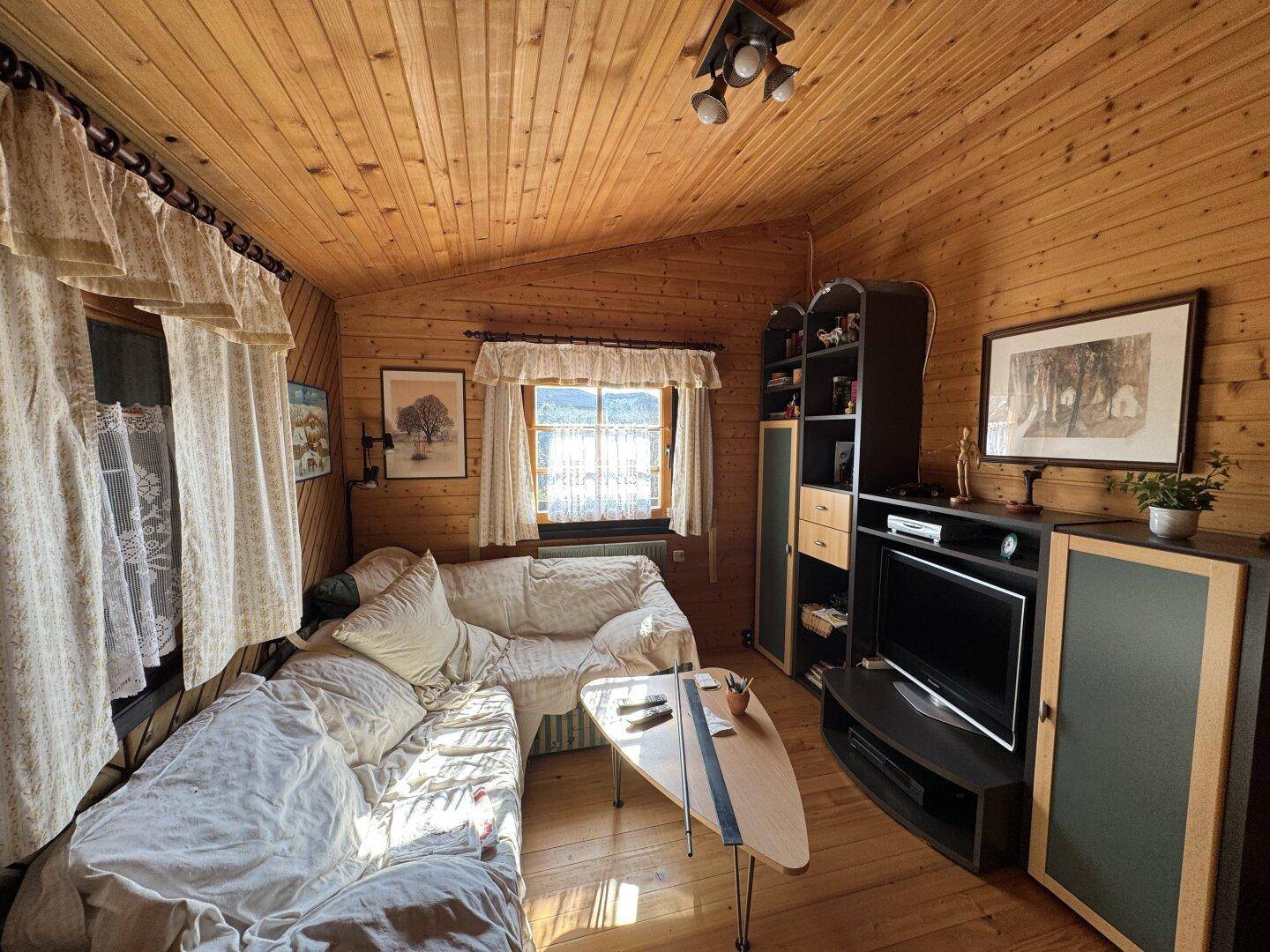 Gemütliches Wohnzimmer mit Holzwänden, Sofa und Fernseher unter einer schrägen Dachgeschossdecke.