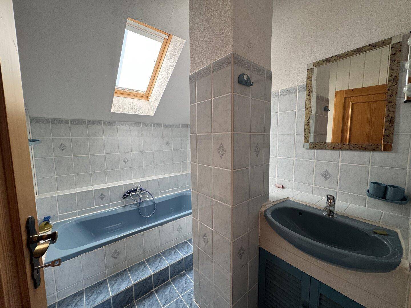 Badezimmer im Dachgeschoss mit blauer Badewanne, Fliesen und einem praktischen Dachfenster.