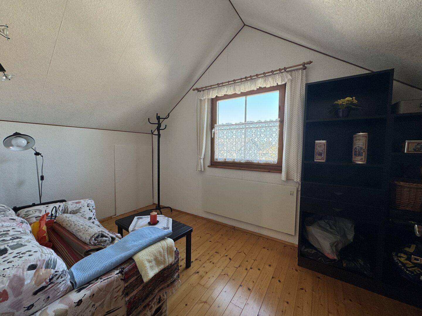 Heller Wohnraum im Dachgeschoss mit Sofa, Regal und Fenster mit traditionellen Gardinen.